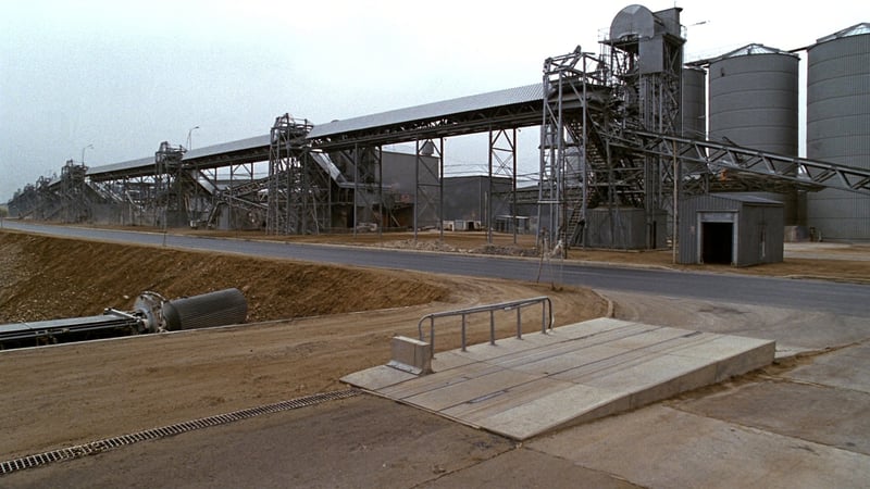The exit road of a mineral processing plant, conveyor galleries and silos behind a concrete weighbridge platform