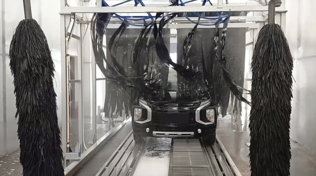 Conveyor tunnel brushes closing over the front of a car on the conveyor