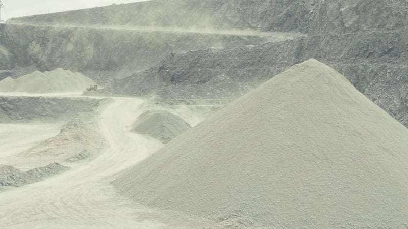 Conical stockpiles of graded crushed stone in a quarry, stepped rock faces rising behind