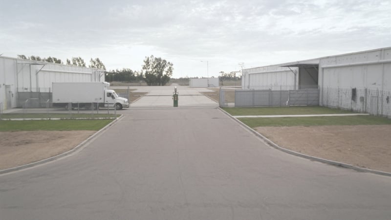 A plain white delivery truck approaching the gated biosecurity checkpoint of a food processing facility