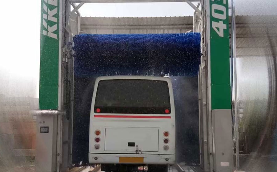 A KKE 403 bus wash gantry mid-cycle: its roof brush turning the length of a white bus roof with water running off both sides of the vehicle, the KKE mark on one column of the machine and the model number 403 on the other