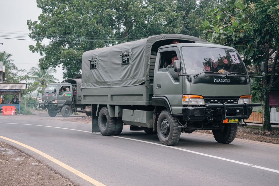 Military utility trucks moving along a rural road — the vehicle class a deployable wash rack serves