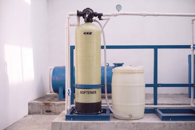 KKE W100 resin water softener installed in a plant room, brine line running from the multiport valve to the brine tank alongside
