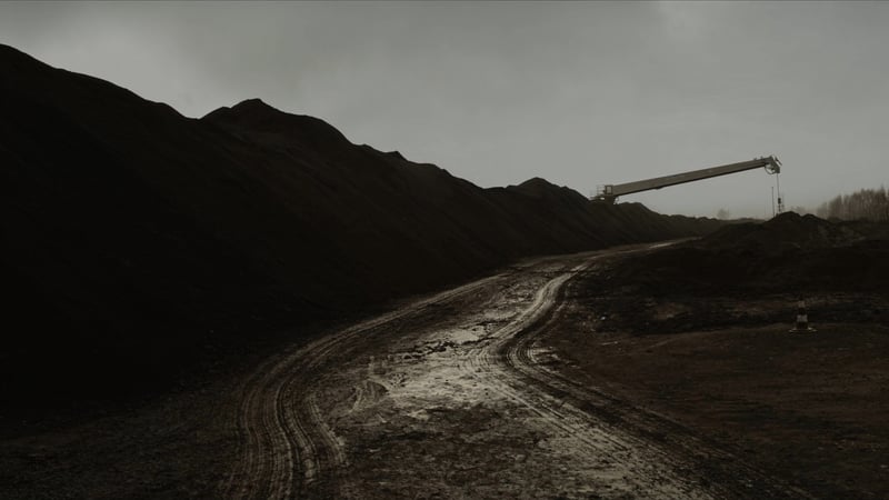 A black coal stockpile with a stacker-reclaimer boom over it and a wet tracked access road alongside