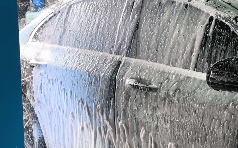 Foam soap sheeting down the flank of a car inside a KKE ArrowClean bay