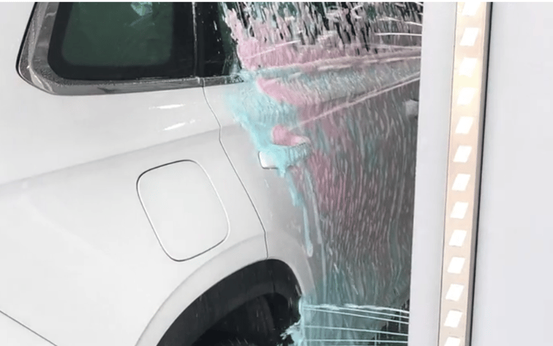 Coloured foam wax running down the side of a white SUV inside a KKE ArrowClean bay