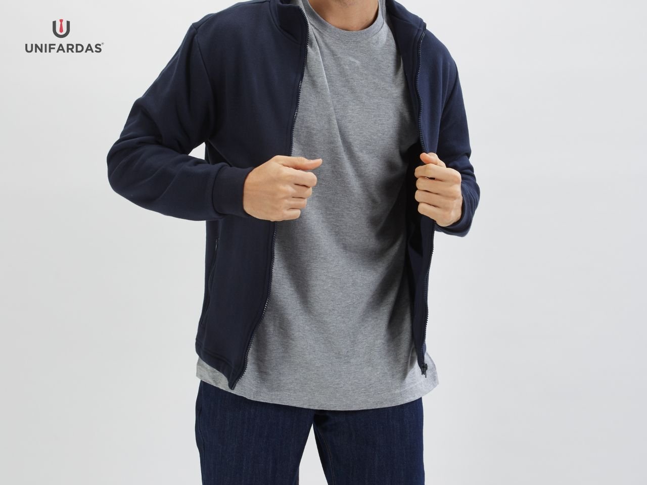 Homem vestido com umas calças de ganga, uma t-shirt cinza e um casaco polar azul marinho para ser usado como farda de trabalho da unifardas