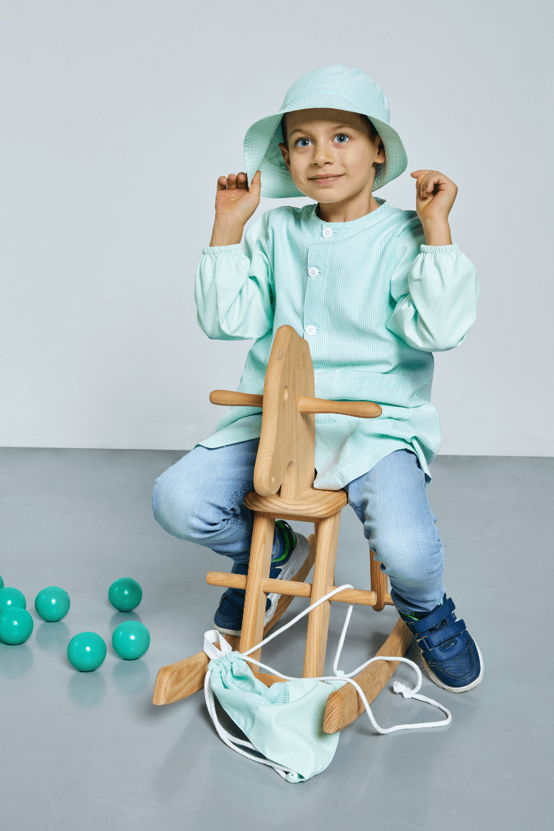 Menino vestido com uma bata para escola da cor verde para uniforme