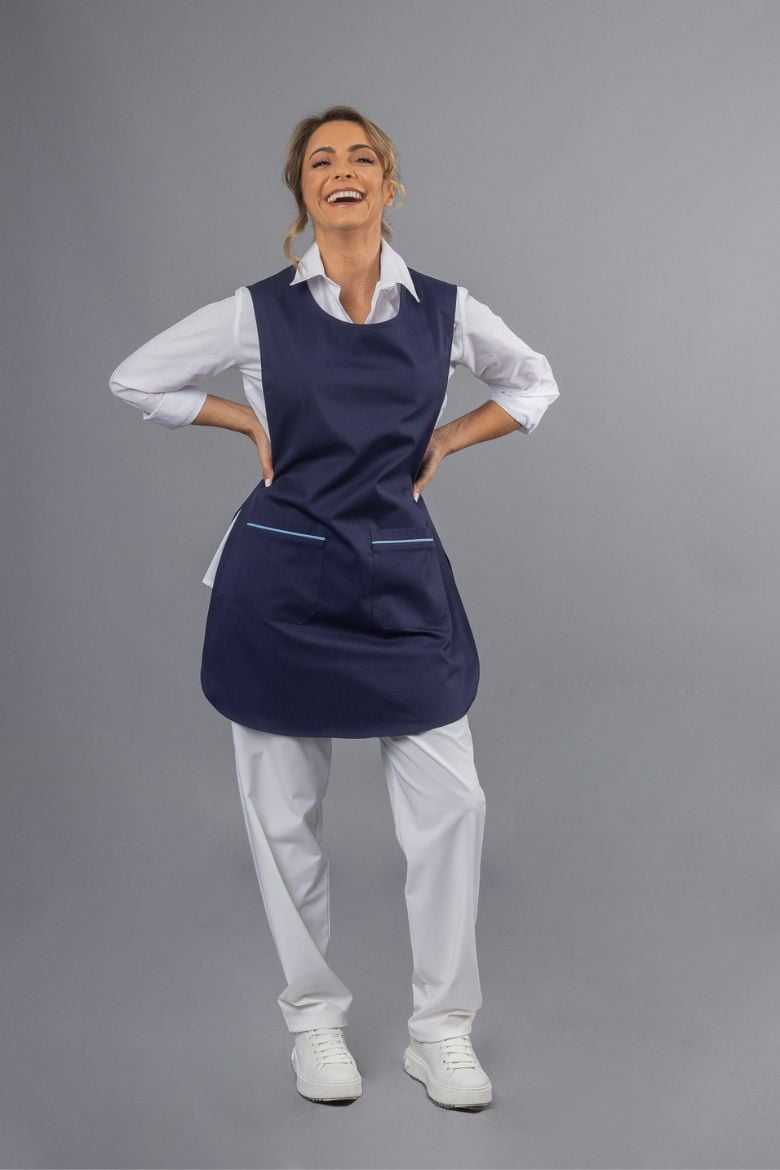 A woman wearing a Women's Professional Uniform Apron Gown in navy blue with blue contrasts on the pocket hems, manufactured by Unifardas