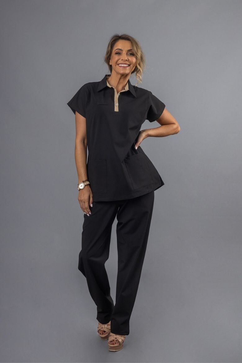 A woman wearing a black tunic with a beige contrast on the collar and black trousers, intended to be worn as a Women's Black Tunic for a professional uniform in the health and wellness work sector.