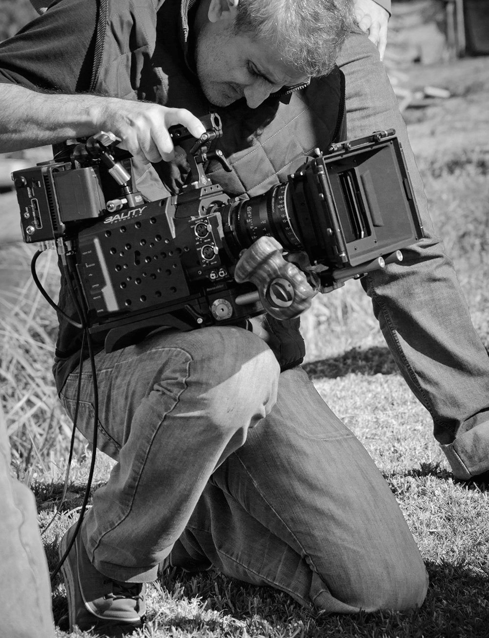 Arturo Marinho, cinematographer, crouching as he operates a cinema camera on location.