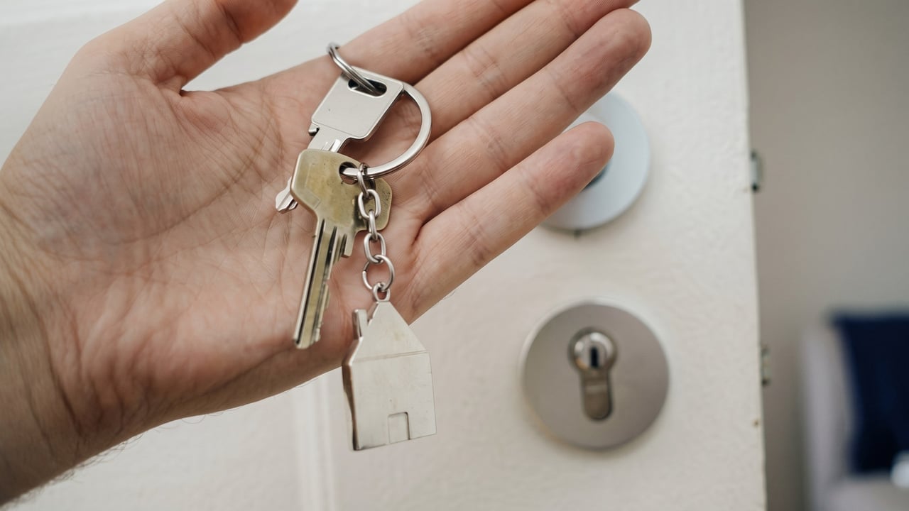 House keys held up beside a deadbolt on a front door