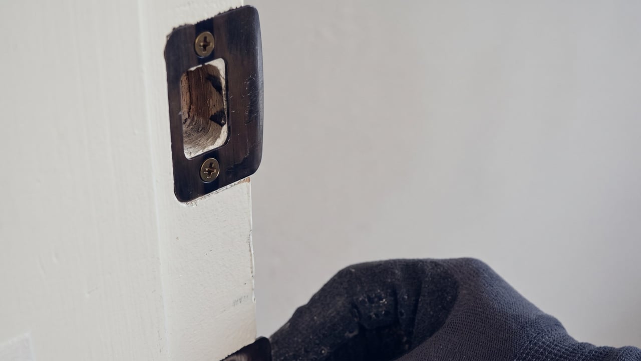 Locksmith in work gloves fitting a strike plate into a door jamb