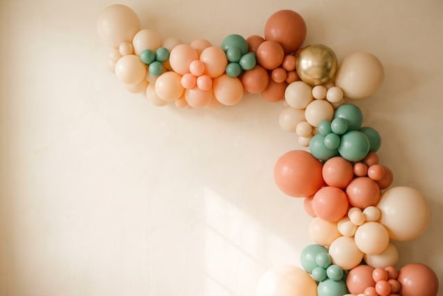 Balloon garland turning a corner in peach, terracotta, sage and gold against a cream plaster wall