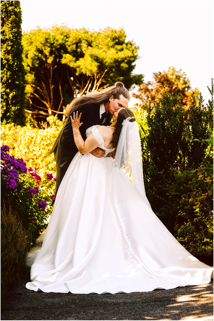 Bride and groom sharing a kiss outdoors in a garden, bride in a white gown and veil, groom in a dark suit