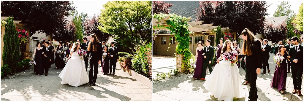 Bride in a white gown with a pink bouquet walks with the groom as bridesmaids in burgundy and groomsmen in black follow along a sunlit garden path.