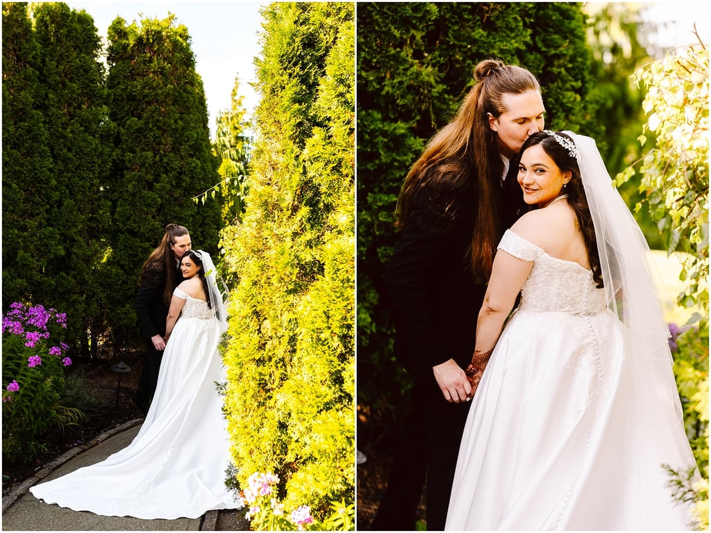 Bride in a white wedding gown and veil with groom kissing her head in a garden.