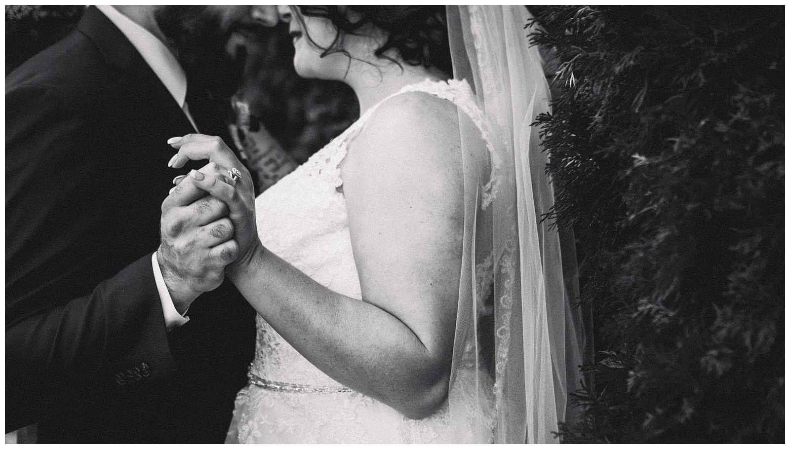 Premier Snohomish & Seattle Wedding Photographer | GSquared Weddings Photography Black-and-white photo of a bride and groom holding hands while dancing at their Snohomish wedding, with the bride in a lace dress and veil, and the groom wearing a suit. Their faces are partially visible and close together. 47.9129° N, 122.0982° W | Serving Snohomish, Seattle , Orlando & Beyond