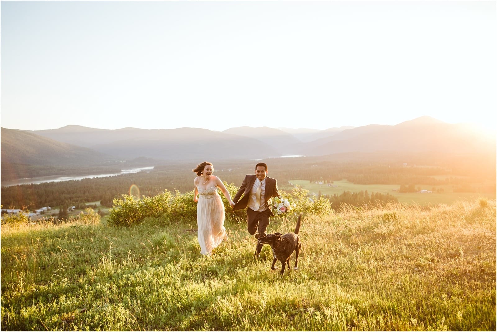Premier Snohomish & Seattle Wedding Photographer | GSquared Weddings Photography A couple in wedding attire runs joyfully with their dog through a sunlit grassy field, surrounded by mountains and a river, capturing the magic of a Snohomish Seattle wedding engagement under a bright, clear sky. 47.9129° N, 122.0982° W | Serving Snohomish, Seattle , Orlando & Beyond