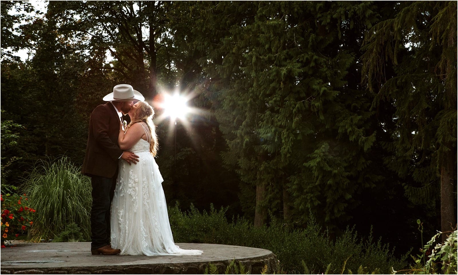 Premier Snohomish & Seattle Wedding Photographer | GSquared Weddings Photography A bride and groom share a kiss on a stone platform surrounded by lush greenery at their Snohomish wedding, sunlight streaming through the trees. The groom wears a cowboy hat; the bride is in a long white dress with loose hair. 47.9129° N, 122.0982° W | Serving Snohomish, Seattle , Orlando & Beyond