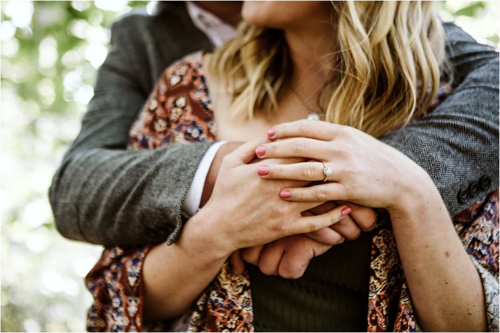 Premier Snohomish & Seattle Wedding Photographer | GSquared Weddings Photography Close-up of a couple embracing outdoors; the woman’s hands, with pink nail polish and an engagement ring, rest atop the man’s arms. Both wear patterned clothing, with lush greenery blurred behind them—perfect for a Snohomish Seattle wedding engagement. 47.9129° N, 122.0982° W | Serving Snohomish, Seattle , Orlando & Beyond