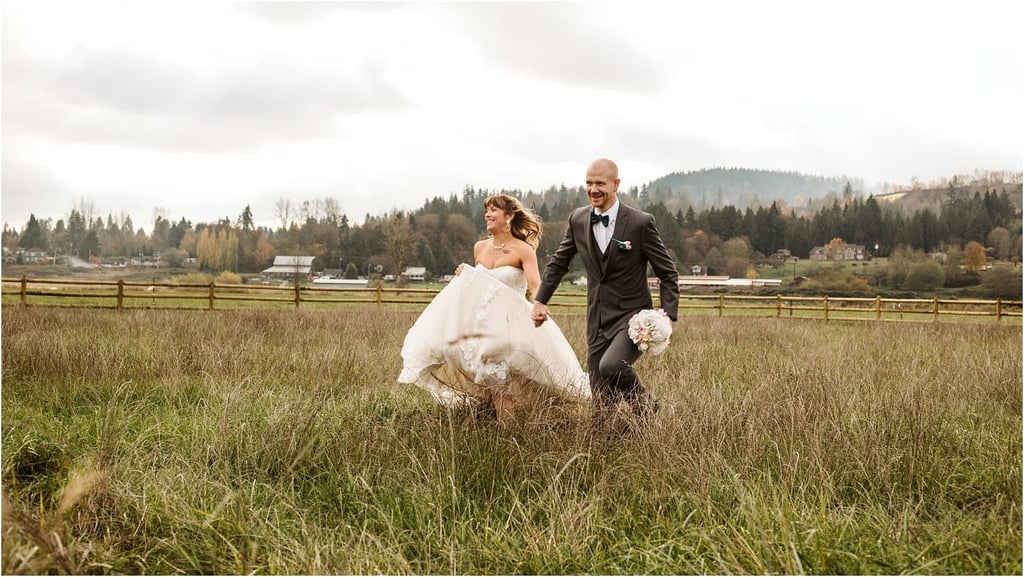 Premier Snohomish & Seattle Wedding Photographer | GSquared Weddings Photography A bride and groom smile and run through a grassy field during their Snohomish wedding, with trees and houses in the background under a cloudy sky. The groom holds a bouquet while the bride lifts her dress slightly as they move. 47.9129° N, 122.0982° W | Serving Snohomish, Seattle , Orlando & Beyond