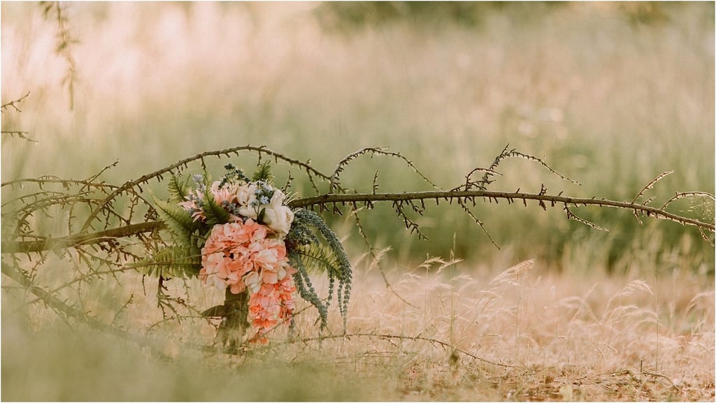 Premier Snohomish & Seattle Wedding Photographer | GSquared Weddings Photography A bouquet of pink and white flowers with greenery rests against a thorny branch in a sunlit, grassy field, creating a soft, dreamy atmosphere—perfect for a Snohomish or Seattle wedding engagement. 47.9129° N, 122.0982° W | Serving Snohomish, Seattle , Orlando & Beyond