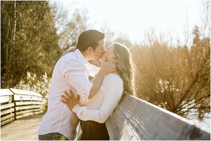 Premier Snohomish & Seattle Wedding Photographer | GSquared Weddings Photography A couple stands on a wooden bridge near Snohomish, kissing passionately in the sunlight. The background features leafless trees and a golden sky, creating a romantic atmosphere perfect for a Seattle wedding engagement. 47.9129° N, 122.0982° W | Serving Snohomish, Seattle , Orlando & Beyond