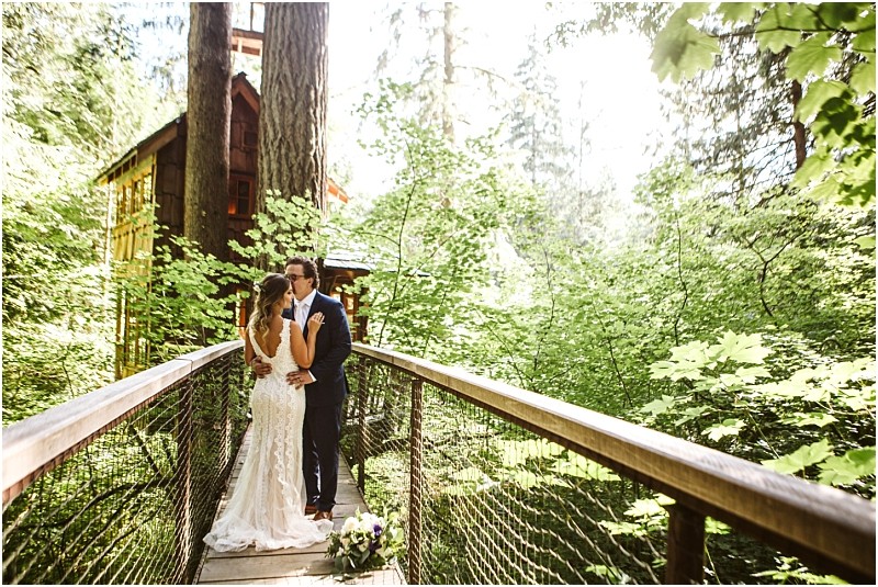 Premier Snohomish & Seattle Wedding Photographer | GSquared Weddings Photography A bride and groom embrace and kiss on a wooden bridge surrounded by lush green trees at a dreamy Snohomish wedding, with a treehouse and sunlight filtering through the forest in the background. 47.9129° N, 122.0982° W | Serving Snohomish, Seattle , Orlando & Beyond