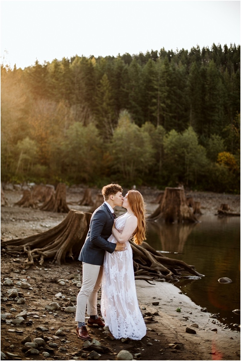 Premier Snohomish Seattle Wedding Photographer | GSquared Weddings Photography A couple dressed in formal attire embraces and kisses on a rocky lakeshore near Snohomish with tree stumps and a dense pine forest in the background The soft light suggests either sunrise or sunset capturing a romantic Seattle wedding engagement moment 479129° N 1220982° W | Serving Snohomish Seattle Orlando Beyond Premier Snohomish & Seattle Wedding Photographer | GSquared Weddings Photography A couple dressed in formal attire embraces and kisses on a rocky lakeshore near Snohomish with tree stumps and a dense pine forest in the background The soft light suggests either sunrise or sunset capturing a romantic Seattle wedding engagement moment 479129° N 1220982° W | Serving Snohomish Seattle Orlando & Beyond