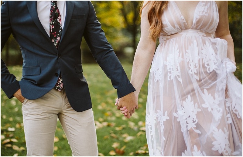 Premier Snohomish & Seattle Wedding Photographer | GSquared Weddings Photography A couple holds hands outdoors during their Snohomish engagement; the person on the left wears a dark blazer, floral tie, and light pants, while the person on the right wears a sheer white dress with floral patterns. Grass and trees are in the background. 47.9129° N, 122.0982° W | Serving Snohomish, Seattle , Orlando & Beyond