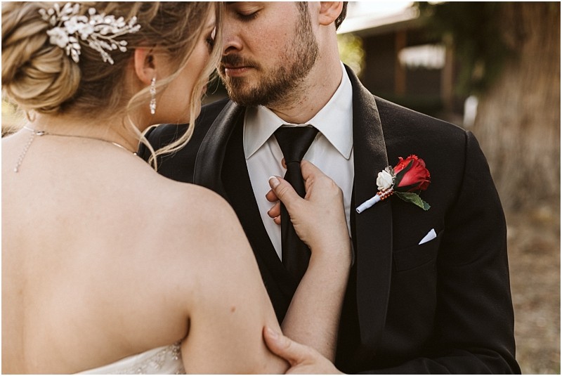 Premier Snohomish & Seattle Wedding Photographer | GSquared Weddings Photography A bride gently holds the groom’s tie as they share an intimate moment during their Snohomish Seattle wedding. The groom wears a black suit with a red rose boutonniere, and the bride’s hair is styled with a decorative hairpiece. 47.9129° N, 122.0982° W | Serving Snohomish, Seattle , Orlando & Beyond