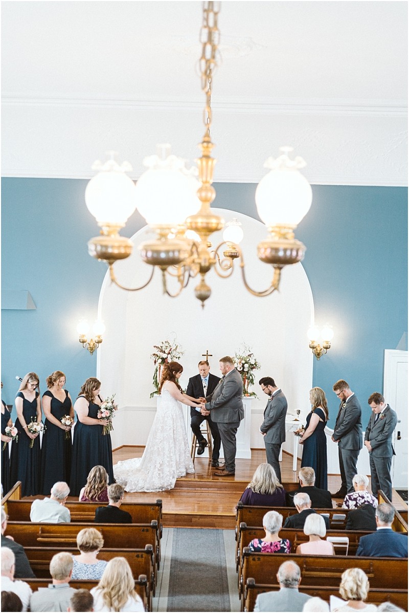Premier Snohomish & Seattle Wedding Photographer | GSquared Weddings Photography A Snohomish wedding ceremony in a church with a bride and groom at the altar, surrounded by their bridal party. Guests are seated in pews, and a chandelier hangs from the ceiling above this beautiful Seattle engagement scene. 47.9129° N, 122.0982° W | Serving Snohomish, Seattle , Orlando & Beyond
