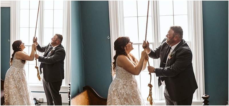 Premier Snohomish & Seattle Wedding Photographer | GSquared Weddings Photography A smiling bride and groom stand by tall windows in a teal room, pulling a large rope together—possibly ringing a bell—during their Snohomish wedding. The bride wears a white lace dress and the groom dons a gray suit. 47.9129° N, 122.0982° W | Serving Snohomish, Seattle , Orlando & Beyond