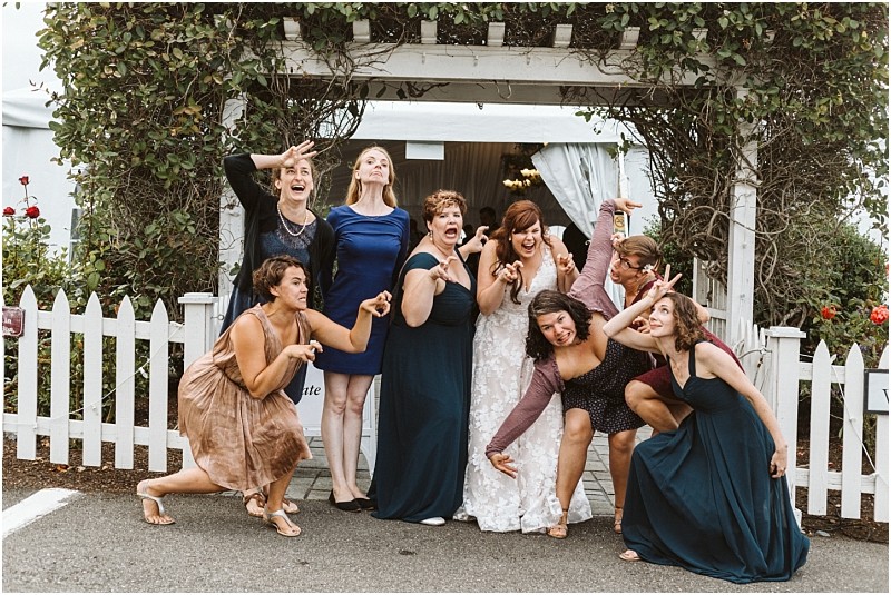 Premier Snohomish & Seattle Wedding Photographer | GSquared Weddings Photography A bride and eight women in dresses pose playfully, making silly faces under a vine-covered arbor at a Snohomish wedding, in front of a white picket fence during an outdoor event. 47.9129° N, 122.0982° W | Serving Snohomish, Seattle , Orlando & Beyond