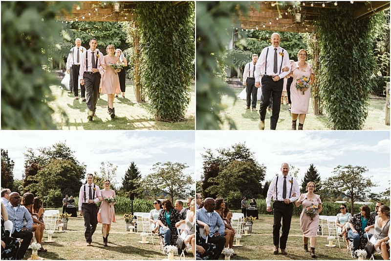 Premier Snohomish & Seattle Wedding Photographer | GSquared Weddings Photography A man and a woman in semi-formal attire walk arm in arm down an outdoor aisle at a Snohomish wedding ceremony, smiling as seated guests watch them. The lush Seattle-area setting features beautiful greenery and flowers. 47.9129° N, 122.0982° W | Serving Snohomish, Seattle , Orlando & Beyond
