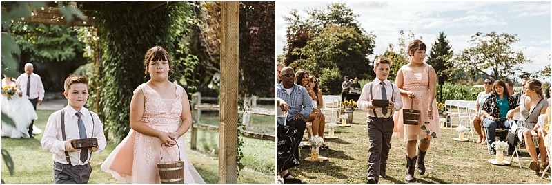 Premier Snohomish & Seattle Wedding Photographer | GSquared Weddings Photography Two children, a boy in suspenders and a girl in a pink dress, walk down the aisle at a Snohomish wedding ceremony, each carrying a small basket. Guests are seated on either side, with lush greenery surrounding this charming Seattle celebration. 47.9129° N, 122.0982° W | Serving Snohomish, Seattle , Orlando & Beyond