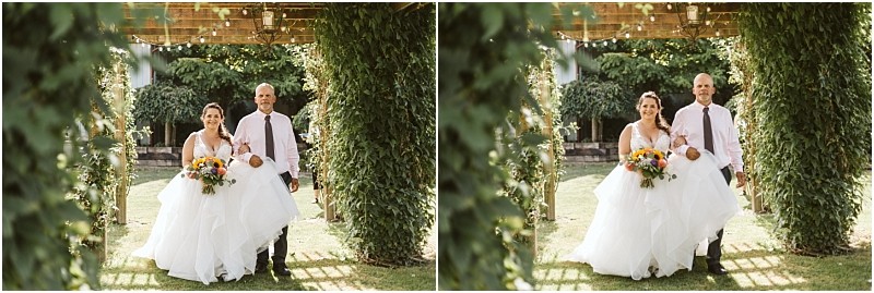 Premier Snohomish & Seattle Wedding Photographer | GSquared Weddings Photography A bride in a white gown holding a colorful bouquet walks arm-in-arm with a man in a light shirt and tie under a vine-covered arbor at an outdoor Snohomish wedding. Both are smiling, surrounded by lush greenery. 47.9129° N, 122.0982° W | Serving Snohomish, Seattle , Orlando & Beyond