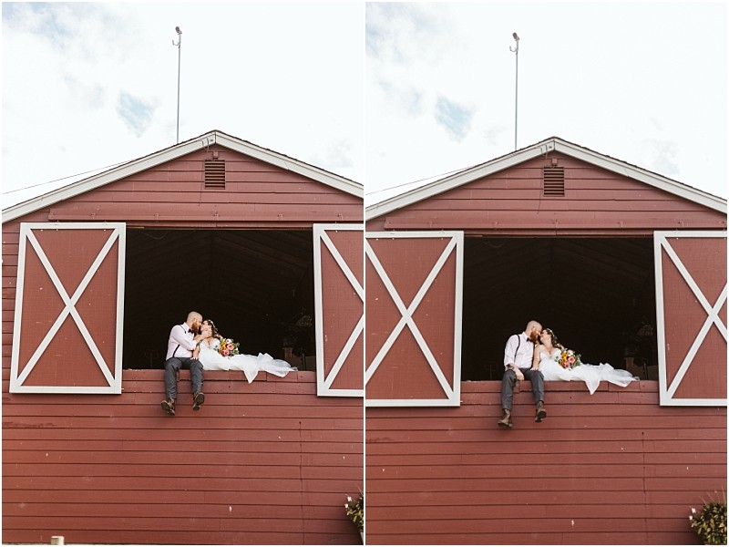 Premier Snohomish & Seattle Wedding Photographer | GSquared Weddings Photography A bride and groom sit in the open window of a red barn at their Snohomish wedding, sharing a kiss and holding a bouquet. The bride’s white dress cascades over the edge, with a partly cloudy sky above them. 47.9129° N, 122.0982° W | Serving Snohomish, Seattle , Orlando & Beyond