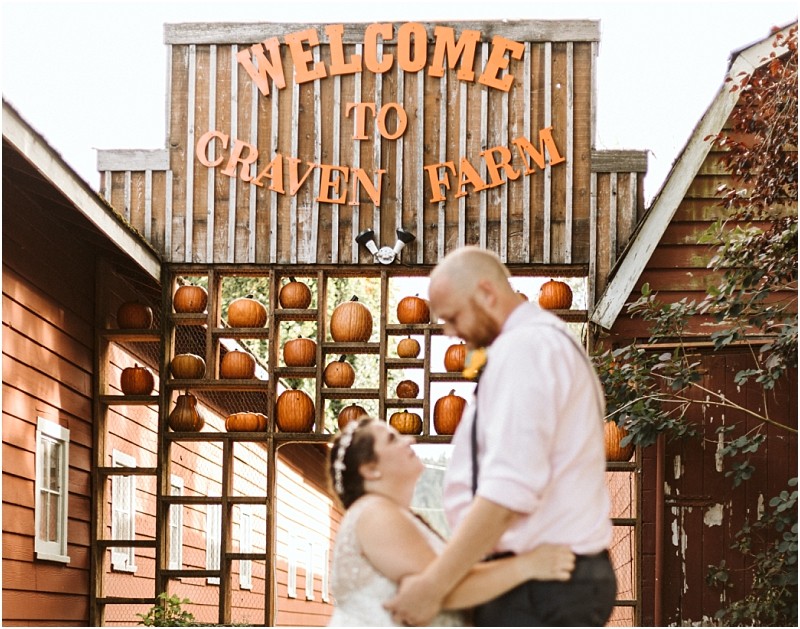 Premier Snohomish & Seattle Wedding Photographer | GSquared Weddings Photography A couple embraces and smiles at the rustic Craven Farm entrance in Snohomish, perfect for a Seattle wedding engagement, with pumpkins displayed on shelves behind them. 47.9129° N, 122.0982° W | Serving Snohomish, Seattle , Orlando & Beyond