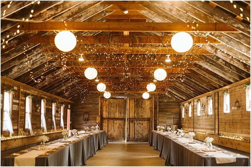 Premier Snohomish & Seattle Wedding Photographer | GSquared Weddings Photography A rustic barn interior in Snohomish, decorated for a Seattle wedding or engagement, glows with string lights and round lanterns. Long tables with gray tablecloths and simple floral centerpieces line both sides of the room. 47.9129° N, 122.0982° W | Serving Snohomish, Seattle , Orlando & Beyond