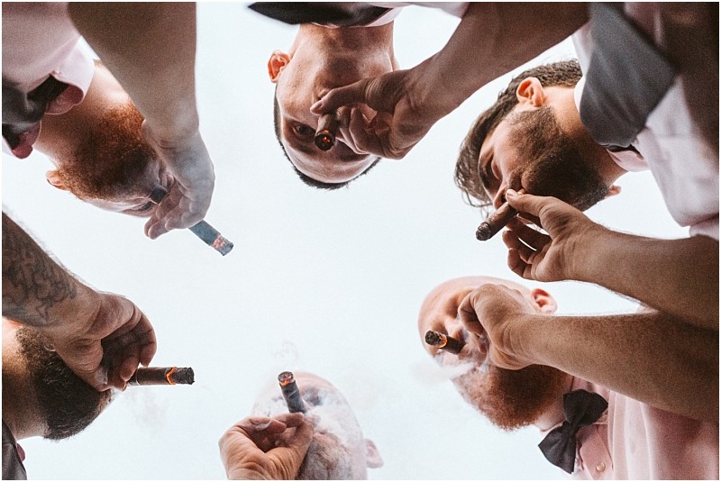 Premier Snohomish & Seattle Wedding Photographer | GSquared Weddings Photography A group of men seen from below, forming a circle and smoking cigars together, with the sky as the background—capturing a candid moment at a Snohomish Seattle wedding engagement. 47.9129° N, 122.0982° W | Serving Snohomish, Seattle , Orlando & Beyond