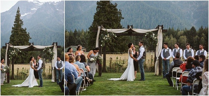 Premier Snohomish & Seattle Wedding Photographer | GSquared Weddings Photography A bride and groom stand under a flower-adorned wooden arch during an outdoor Snohomish wedding ceremony, surrounded by mountains, trees, their wedding party, and seated guests. 47.9129° N, 122.0982° W | Serving Snohomish, Seattle , Orlando & Beyond