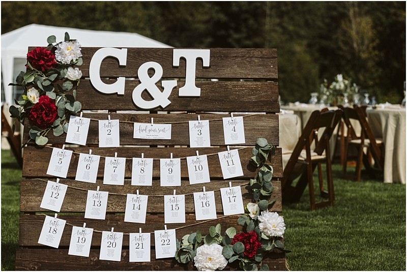 Premier Snohomish & Seattle Wedding Photographer | GSquared Weddings Photography A rustic wooden wedding seating chart, perfect for a Snohomish or Seattle wedding, is adorned with flowers and large white letters C & T. Individual cards display table assignments outdoors, with reception tables and chairs in the background. 47.9129° N, 122.0982° W | Serving Snohomish, Seattle , Orlando & Beyond