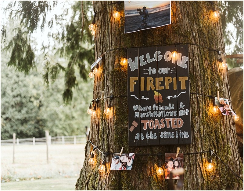 Premier Snohomish & Seattle Wedding Photographer | GSquared Weddings Photography A tree decorated with string lights, photos, and a sign that reads, “Welcome to our firepit. Where friends & marshmallows get toasted at the same time.” The perfect Snohomish or Seattle wedding or engagement backdrop, set in a grassy field with fencing. 47.9129° N, 122.0982° W | Serving Snohomish, Seattle , Orlando & Beyond