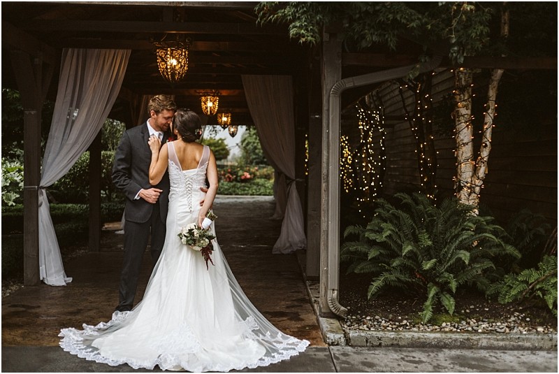 Premier Snohomish & Seattle Wedding Photographer | GSquared Weddings Photography A bride and groom stand close together under a covered outdoor walkway decorated with hanging lights and white drapes at their Snohomish Seattle wedding. The bride holds a bouquet, with fairy lights wrapped around a nearby tree adding to the romance. 47.9129° N, 122.0982° W | Serving Snohomish, Seattle , Orlando & Beyond