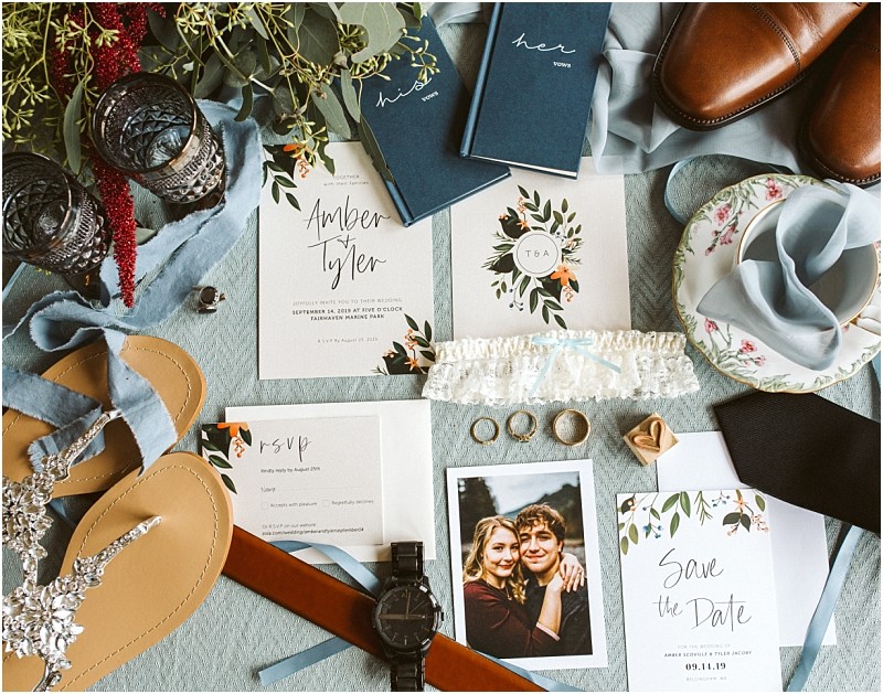 Premier Snohomish & Seattle Wedding Photographer | GSquared Weddings Photography Flat lay of Snohomish wedding items on a light blue surface, featuring invitations, rings, a “Save the Date” card, garter, wristwatch, brown shoes, sandals, blue vow books, a couple’s photo, and floral accents—perfect Seattle engagement inspiration. 47.9129° N, 122.0982° W | Serving Snohomish, Seattle , Orlando & Beyond