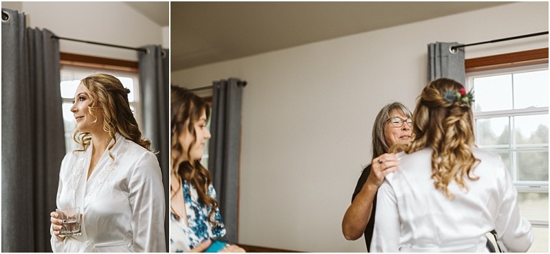 Premier Snohomish & Seattle Wedding Photographer | GSquared Weddings Photography A woman in a white robe holding a glass smiles, while another woman adjusts something near her neckline in a softly lit room with gray curtains and a window—capturing a serene moment before a Snohomish Seattle wedding. 47.9129° N, 122.0982° W | Serving Snohomish, Seattle , Orlando & Beyond