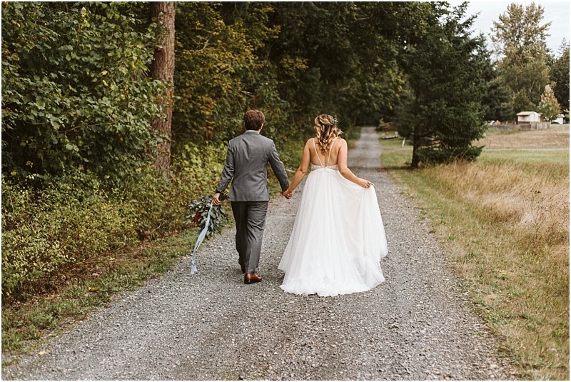 Premier Snohomish & Seattle Wedding Photographer | GSquared Weddings Photography A bride in a white gown and a groom in a gray suit walk hand in hand down a gravel path surrounded by greenery at their Snohomish wedding, with trees and grass lining both sides. 47.9129° N, 122.0982° W | Serving Snohomish, Seattle , Orlando & Beyond