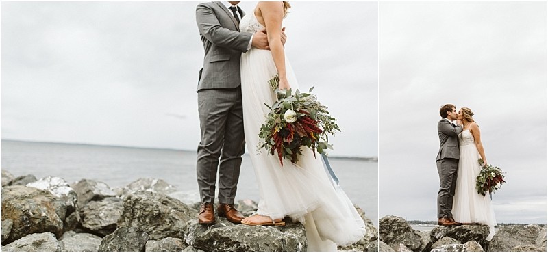Premier Snohomish & Seattle Wedding Photographer | GSquared Weddings Photography A bride and groom share an intimate moment on a rocky shore near the water. The bride holds a bouquet of greenery and burgundy flowers, while the groom wears a gray suit—capturing a romantic Snohomish Seattle wedding scene beneath a cloudy sky. 47.9129° N, 122.0982° W | Serving Snohomish, Seattle , Orlando & Beyond